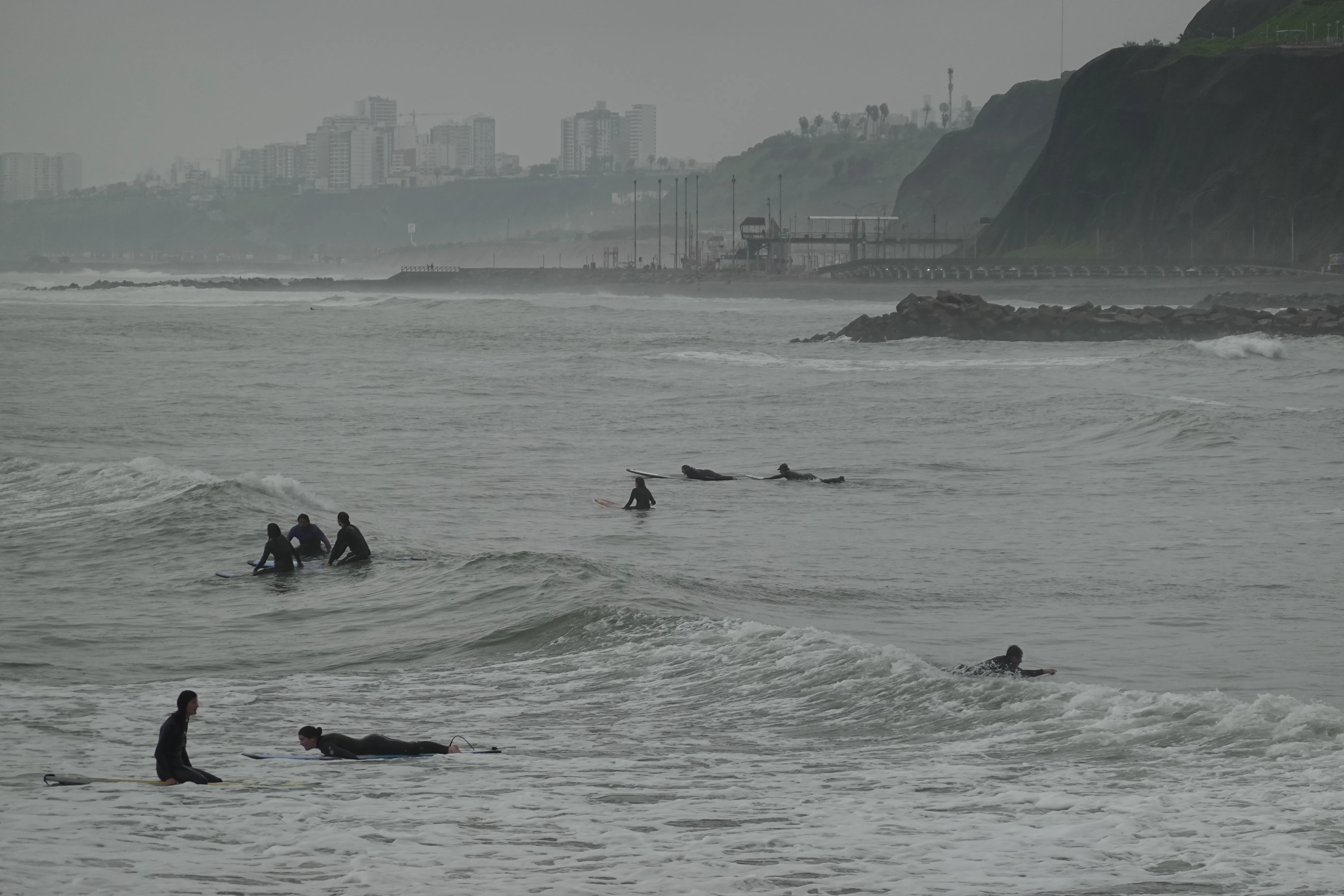 Coast view with surfers and city buildings up on the cliff
